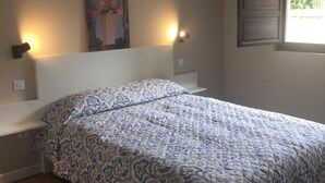 Un dormitorio con una cama grande, vigas de madera en el techo, un cuadro en la pared y una ventana con vistas al verdor.