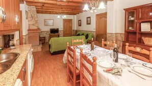 Un coin repas chaleureux avec une table en bois dressée pour quatre personnes, une cheminée en pierre et un téléviseur en arrière-plan.