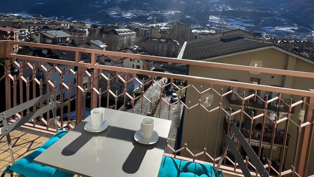 Ein Balkon mit Tisch und Stühlen mit Blick auf eine gebirgige Landschaft.