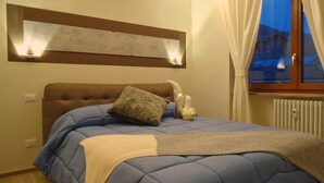Een slaapkamer met een bed, een hoofdbord, een wandlamp en een raam met gordijnen.