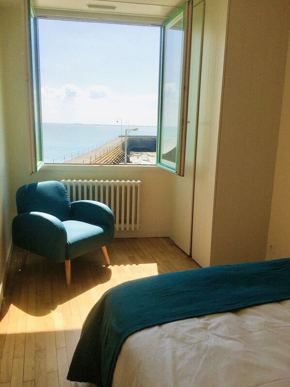 A room with a large window, a blue chair, a bed, and a radiator.