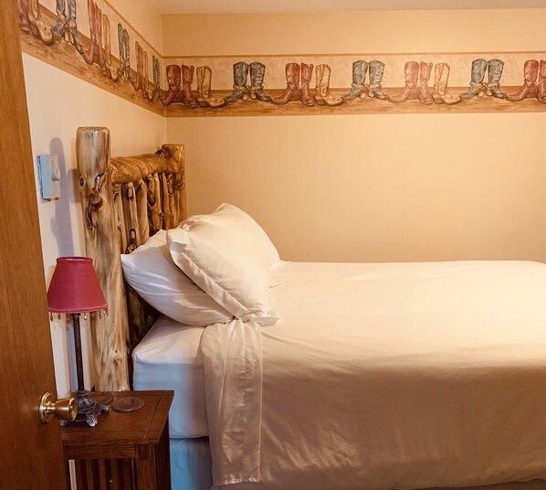 A neatly made bed with white linens, a wooden headboard, a red lamp, and a wooden nightstand with a small table. - Yellowstone/Union Pass Log Cabin Retreat  (Dubois)