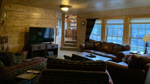 A cozy cabin interior with a television, leather sofa, and a dining area.