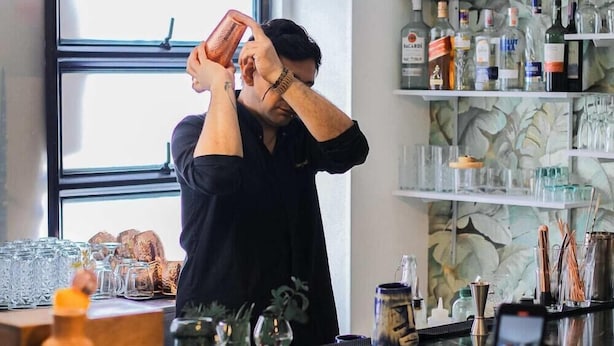 A bar setting with a bartender preparing drinks, shelves with bottles, and a window in the background. - Ayenda 1066 Virrey Centro (Bogotá)