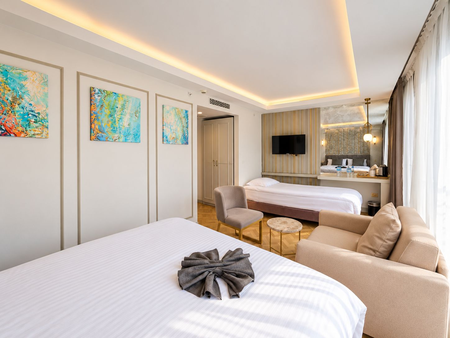 Habitación de hotel con una cama grande, un sofá, una mesita y un televisor. Hay tres cuadros en la pared.