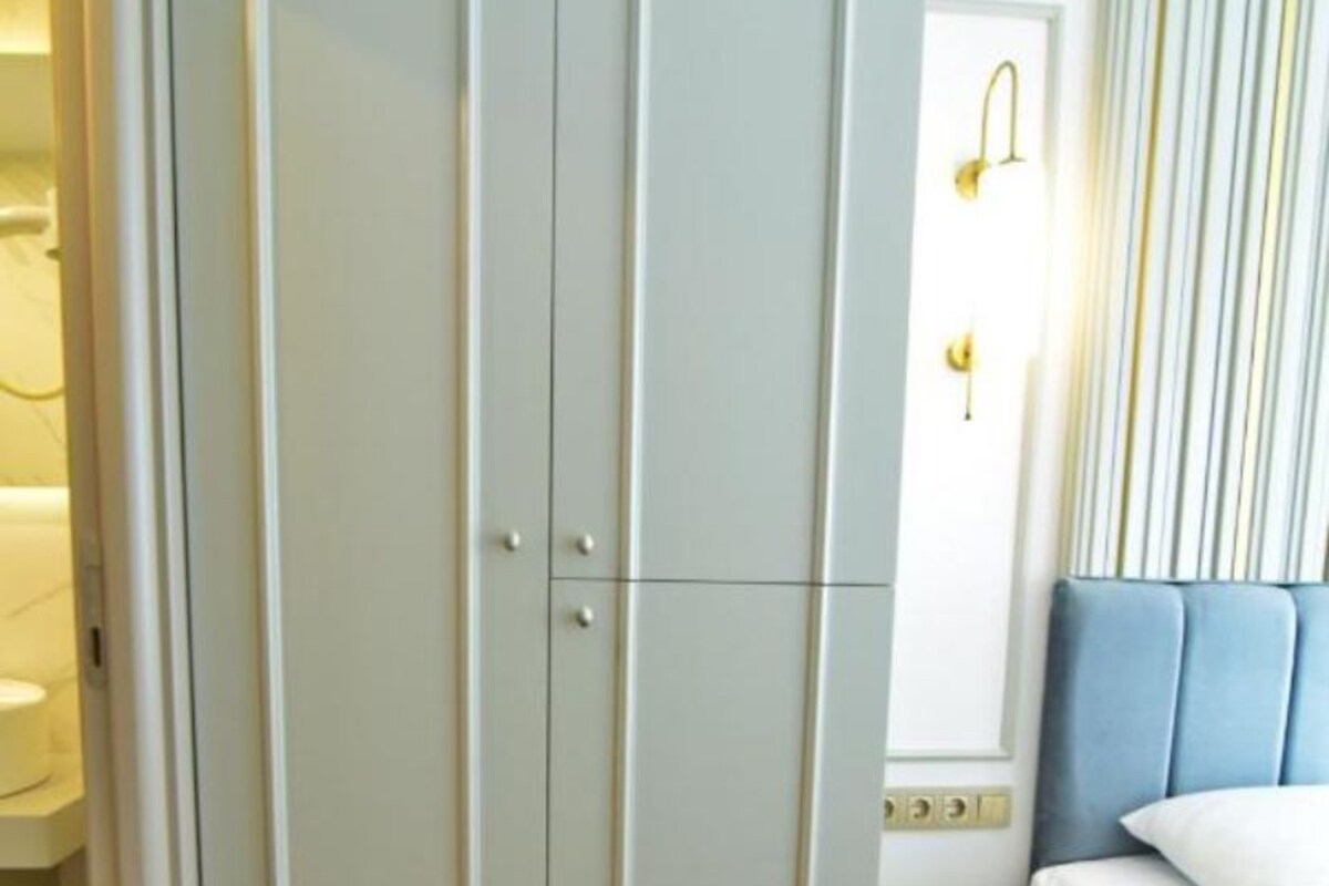 A room with a wardrobe, a bed, and a wall-mounted light fixture.