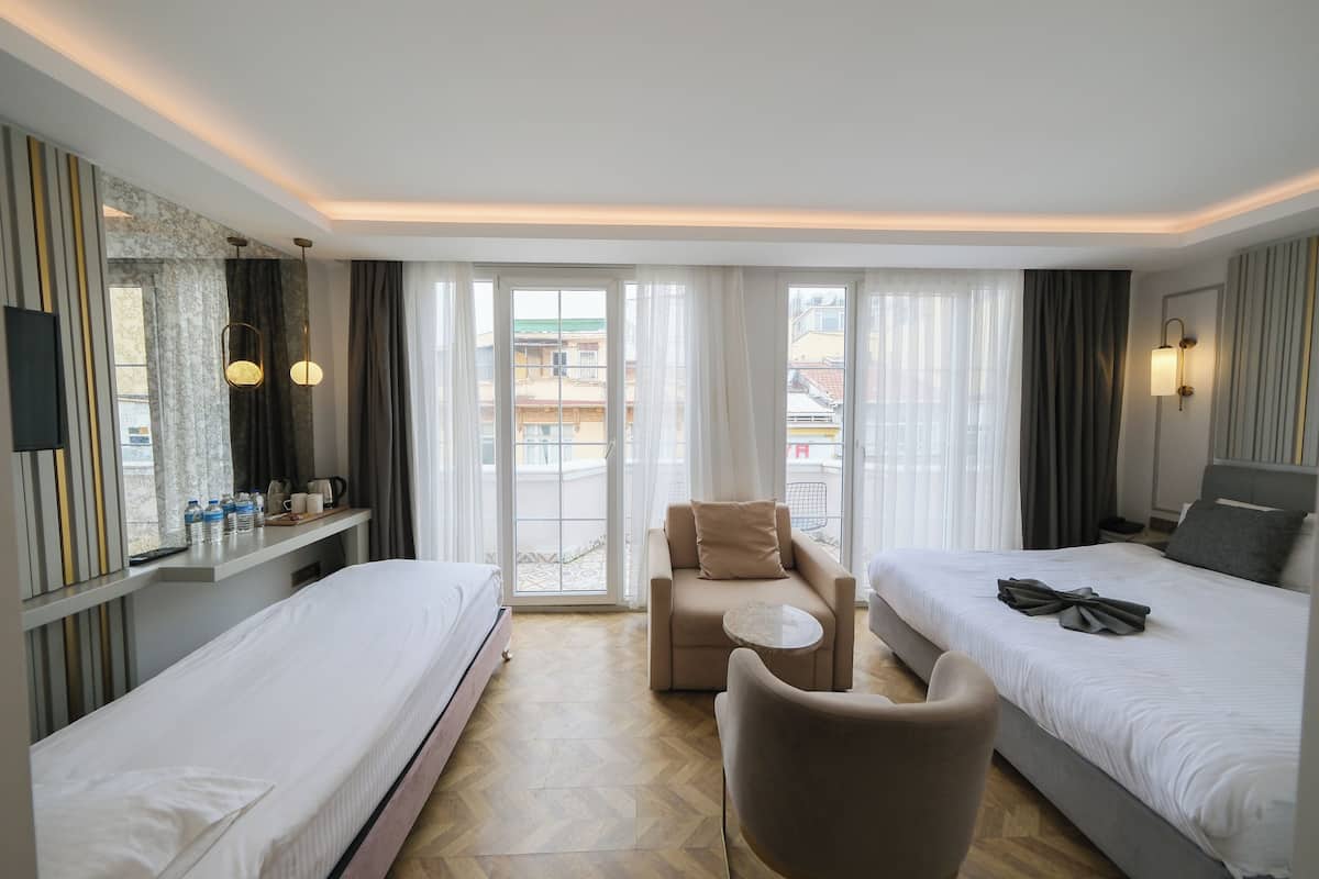 A hotel room with two beds, a sofa, a small table, and a balcony with a view.