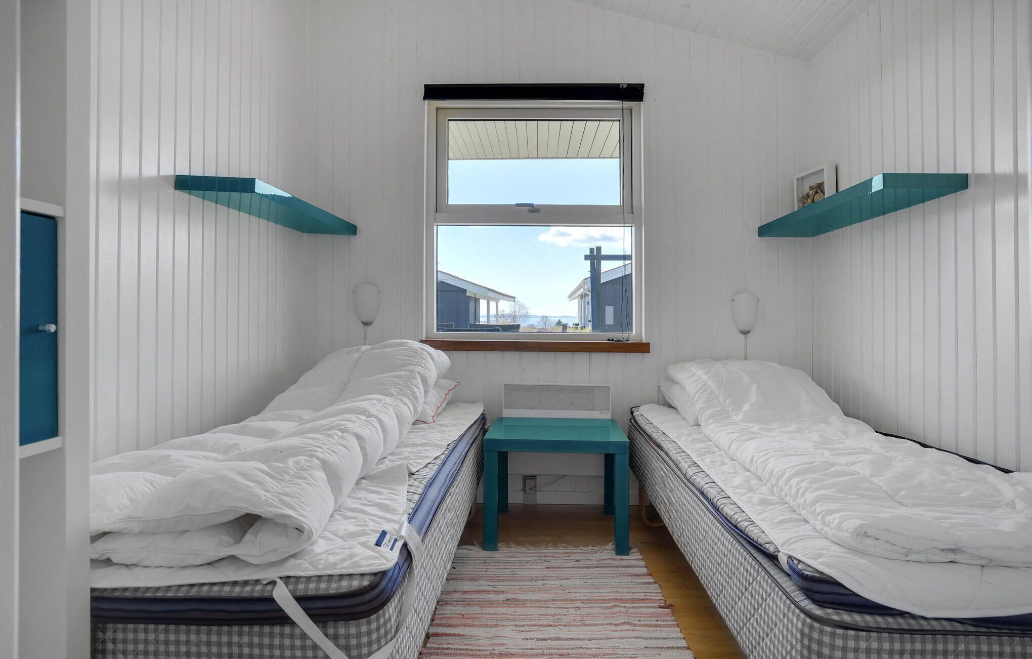 Un petit logement composé d’une seule pièce, comprenant deux lits simples, une fenêtre donnant sur des immeubles et une petite table placée au centre.