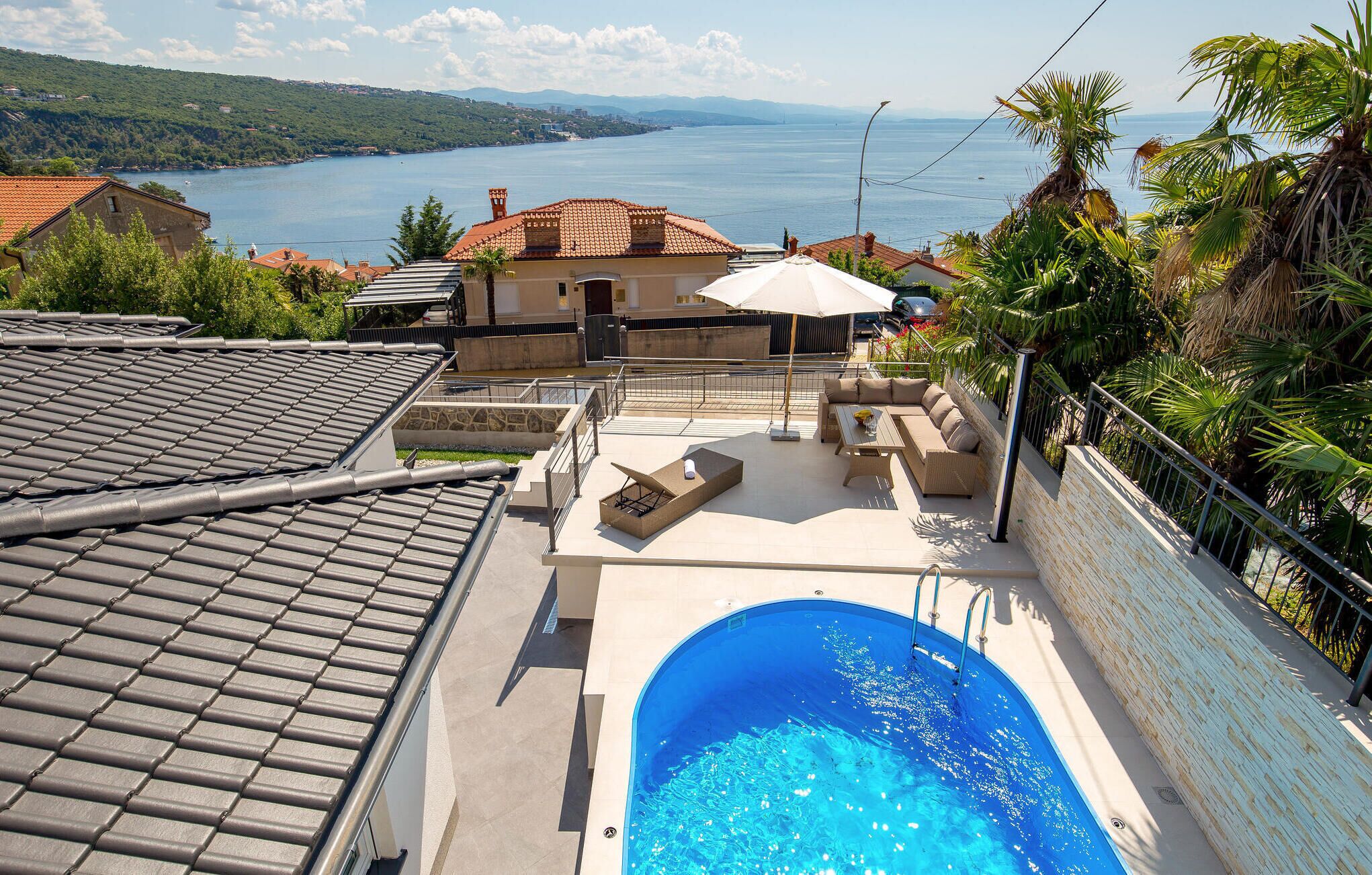 Una piscina en la azotea con vista al mar, mobiliario exterior y un muro de piedra.