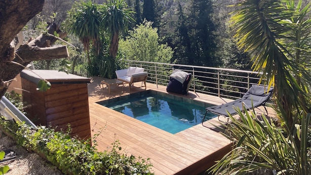 Een houten terras met een zwembad, ligbedden en een kleine houten constructie, omgeven door groen en heuvels.