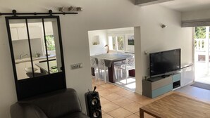 Een woonkamer met een bank, een televisie, een houten salontafel en een speaker. Op de achtergrond bevindt zich een eethoek met een tafel en stoelen.