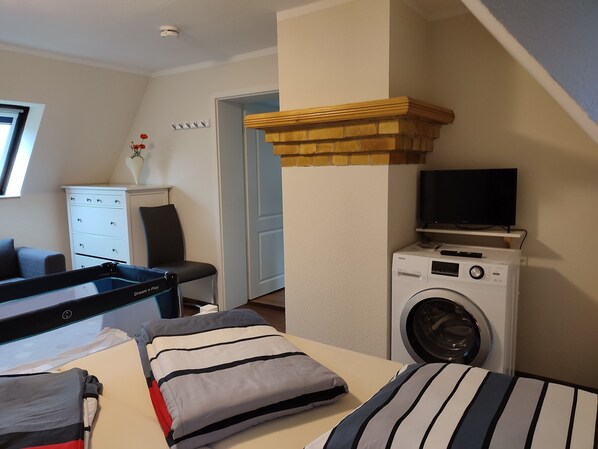 A bedroom with a bed, a washing machine, a television, a dresser, and a window.