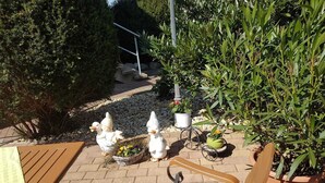 A patio area with a wooden bench, decorative bird sculptures, potted plants, and a stone pathway. - Wunderschöne Ferienwohnung (Brandenburg an der Havel)
