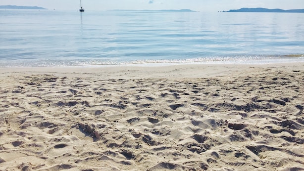 A sandy beach with footprints, calm water, and a sailboat in the distance. - Maison VUE MER 50M DE LA Plage A Pied (Hyères)