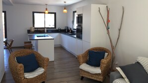 A modern kitchen with white cabinets, a central island, and a dining area with wicker chairs. - Maison VUE MER 50M DE LA Plage A Pied (Hyères)