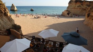 Una playa con acantilados rocosos, una orilla arenosa y mobiliario exterior con sombrillas.