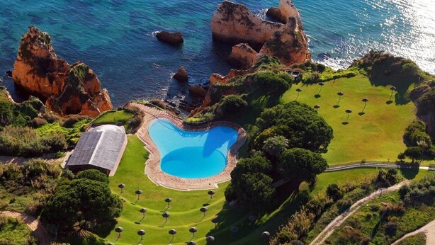 Vista aérea de un campo de golf con una piscina en forma de corazón, rodeado de exuberante vegetación y acantilados rocosos.