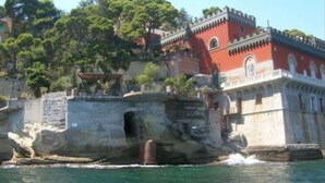 Ein Küstengebäude mit roter Fassade und Steinwänden direkt am Wasser.