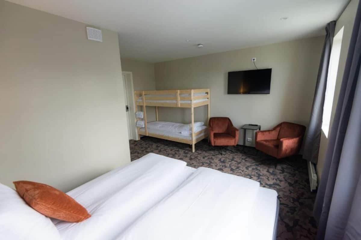 Een hotelkamer met een stapelbed, twee fauteuils, een kleine tafel en een televisie aan de muur.