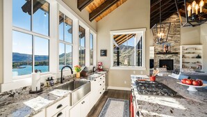 A kitchen with large windows, a stone fireplace, and a view of a lake.