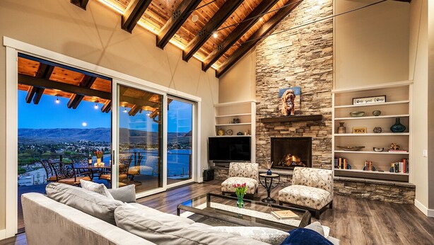 A spacious living room with a stone fireplace, comfortable seating, and a large glass door leading to a balcony with a city view.