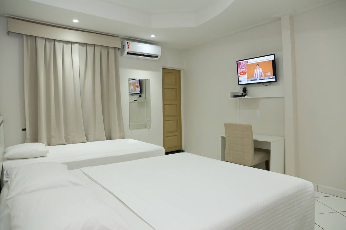 A hotel room with two beds, a TV, an air conditioning unit, and a desk.