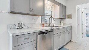 A modern kitchen with grey cabinets, a stainless steel dishwasher, and a marble countertop.