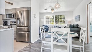 A modern kitchen with stainless steel appliances, a dining area with white chairs, and a ceiling fan.