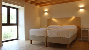 A bedroom with a double bed, wooden flooring, a large window, and two wall-mounted lights.