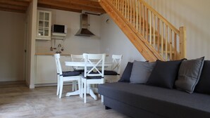 A cozy living area with a wooden staircase, a dining table with chairs, a sofa, and a kitchen area with cabinets and a microwave.