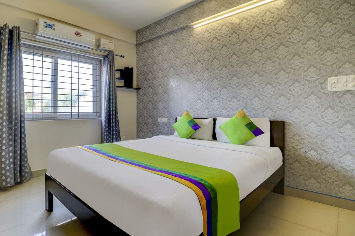 A neatly made bed with a colorful bedspread, a window with curtains, and a patterned wall.