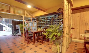 Uma área de refeições com mesa e cadeiras de madeira, cercada por plantas em vasos e um porta-sapatos fixado na parede.