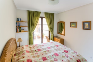 A bedroom with a bed, a nightstand, a lamp, a bookshelf, and a window with curtains.