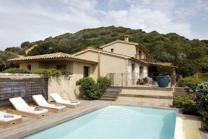 A villa with a swimming pool, lounge chairs, and a patio area.