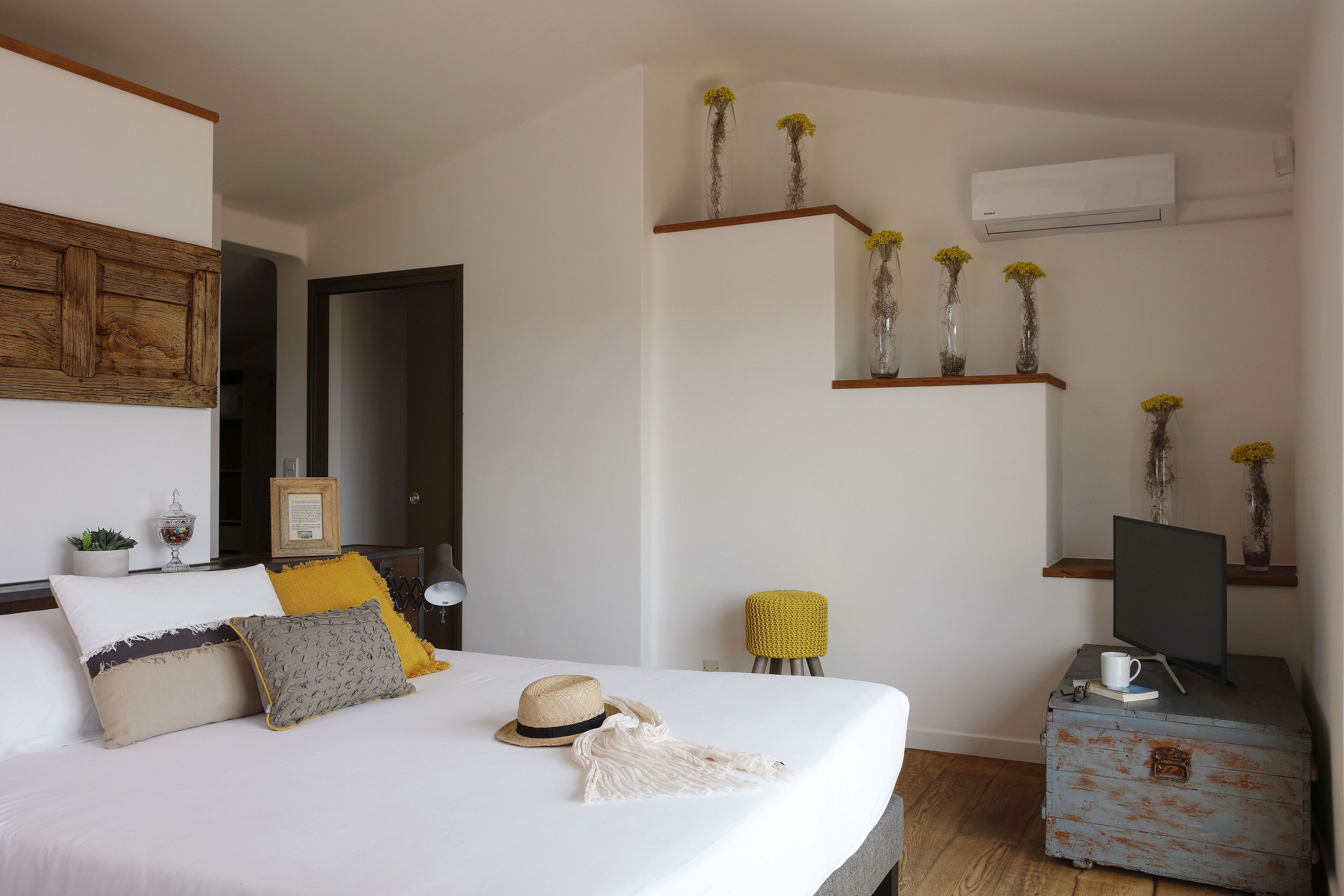 A neatly arranged bedroom with a bed, bedside tables, a mirror, and decorative items like vases and a hat.