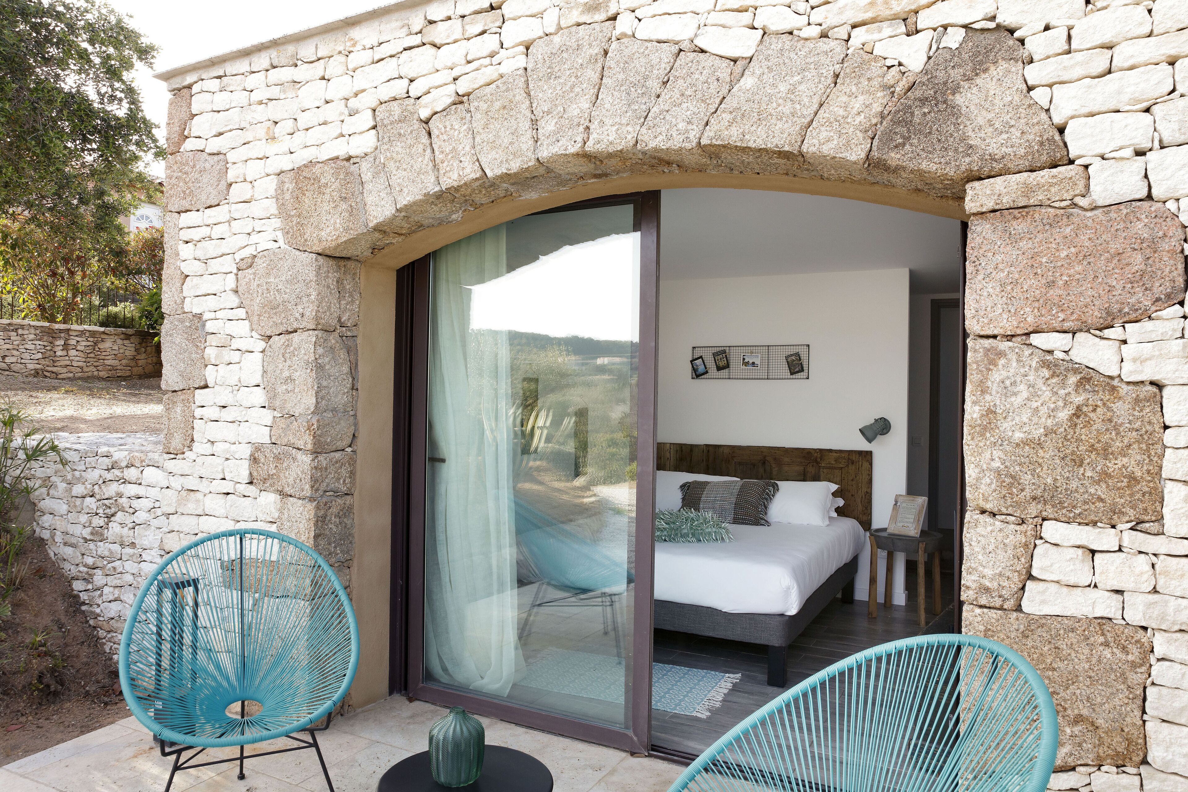A bedroom with a stone facade, a large sliding glass door, and two turquoise chairs.