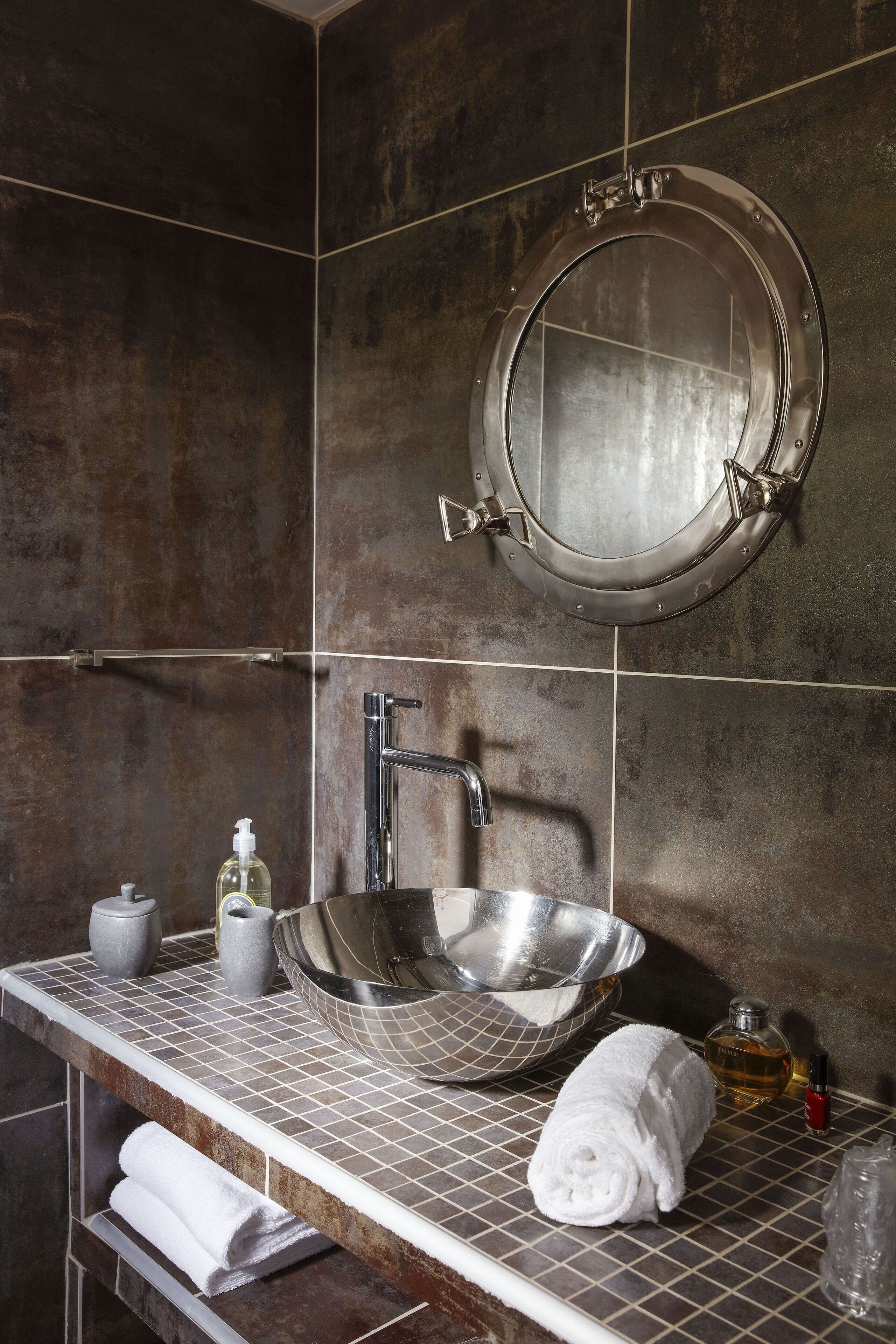 A bathroom with a round mirror, a large sink, and a towel rack.