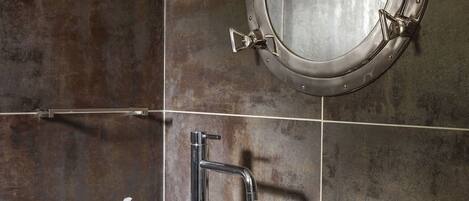 A bathroom with a round mirror, a large sink, and a towel rack.