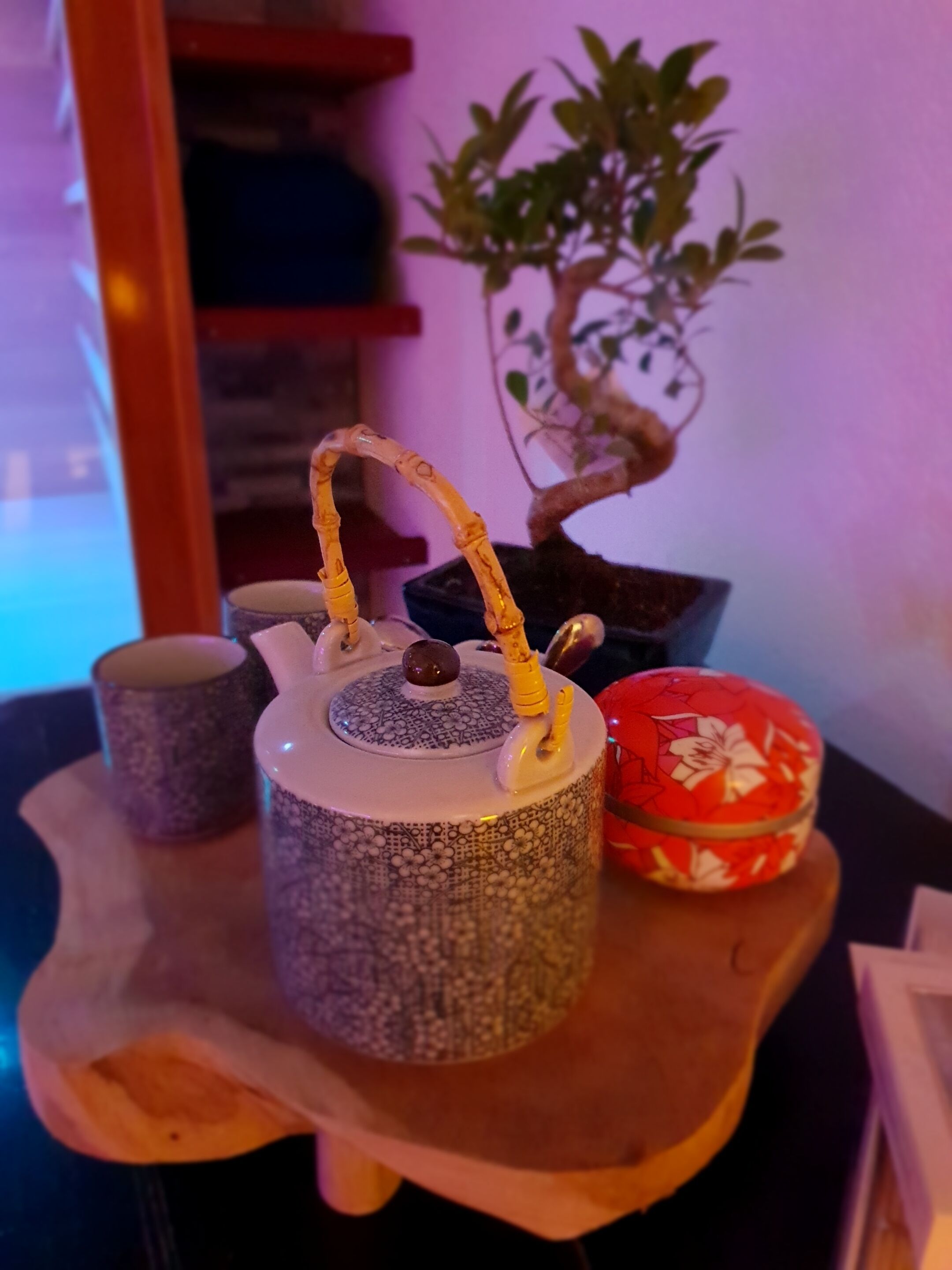 Una teiera in ceramica con manico, una tazza e un contenitore decorativo su un vassoio di legno.