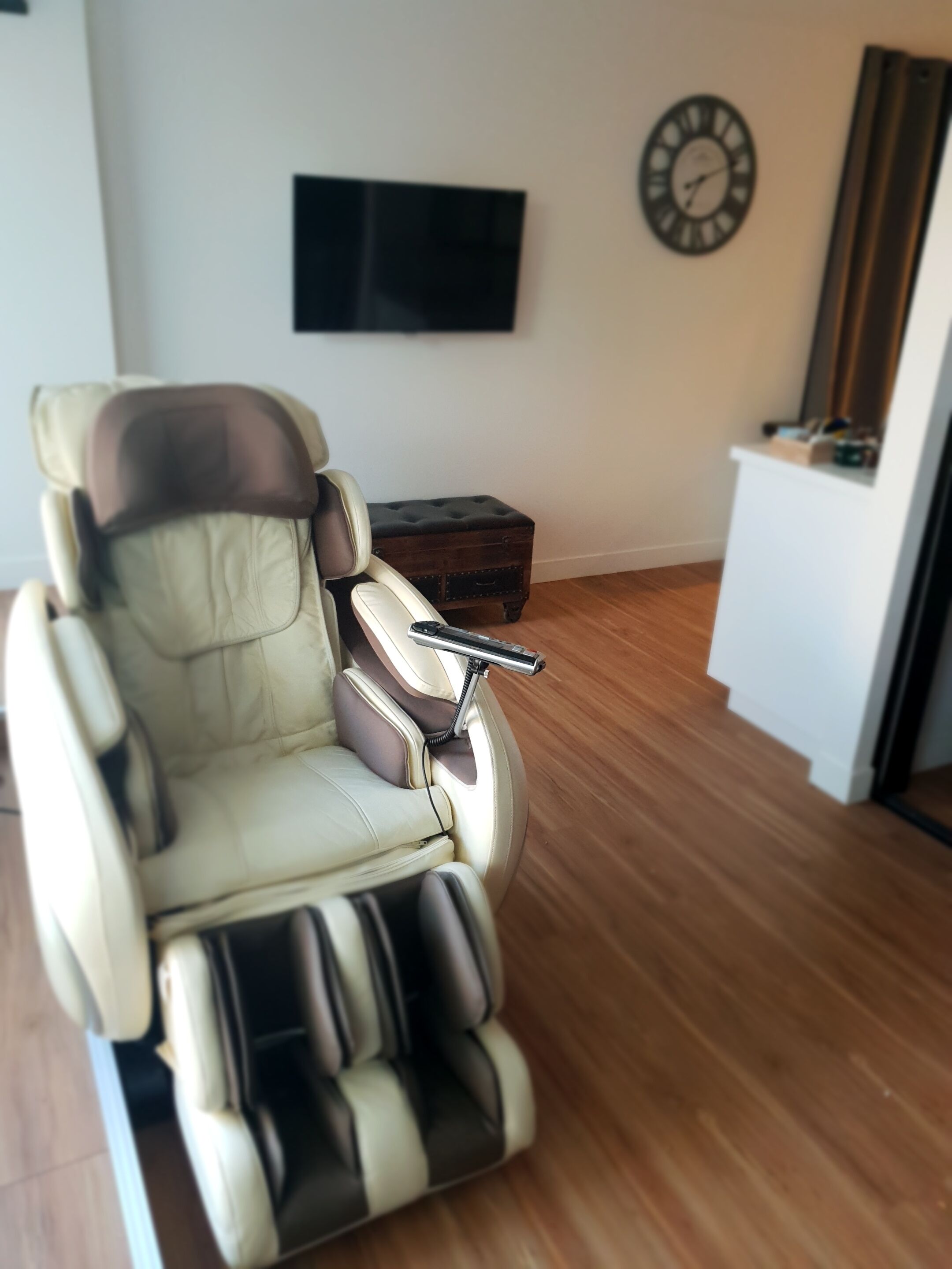 Un salon moderne avec un fauteuil inclinable en cuir, un téléviseur à écran plat, un meuble en bois et une horloge au mur.