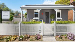 Une petite maison avec une clôture blanche en bois, une porte d’entrée et une enseigne.