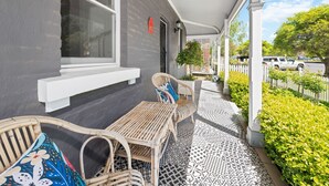 Une véranda couverte avec des meubles en osier, une boîte aux lettres et un sol à motifs.