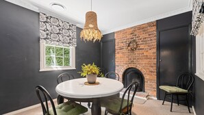 Un coin repas avec une table ronde, des chaises, un luminaire suspendu, une plante en pot et une cheminée en briques.