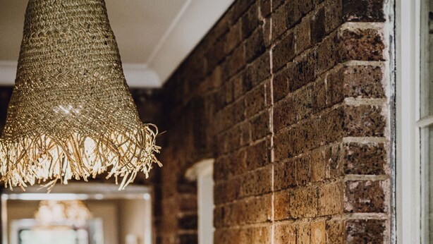 Un couloir avec un luminaire en fibres tressées, des murs en briques et une porte.