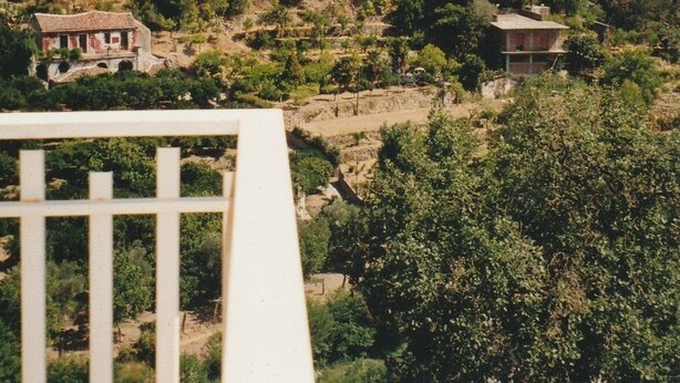 Paisagem montanhosa com edifícios e vegetação dispersos.