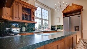A kitchen with wooden cabinets, a large island, a stainless steel refrigerator, and a window providing natural light. - Carnegie Library Shakespeare Apartment 3 bed (Swinton)
