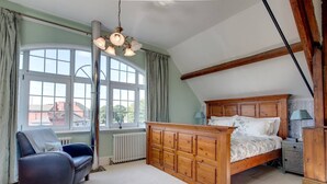 A bedroom with a wooden bed, a chair, a radiator, and a window with curtains. - Carnegie Library Shakespeare Apartment 3 bed (Swinton)