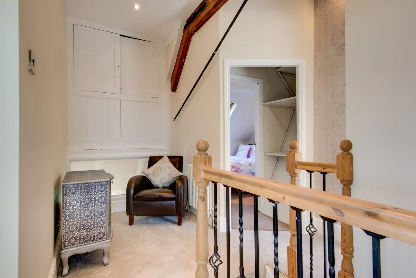 A staircase with a wooden handrail leading to a bedroom with a bed and a chair.