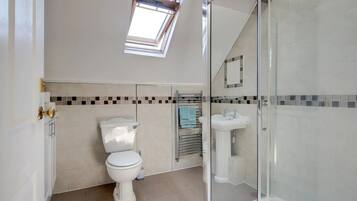 Een moderne badkamer met toilet, wastafel en douche. Boven het toilet bevindt zich een dakraam en de douche is omgeven door glas.