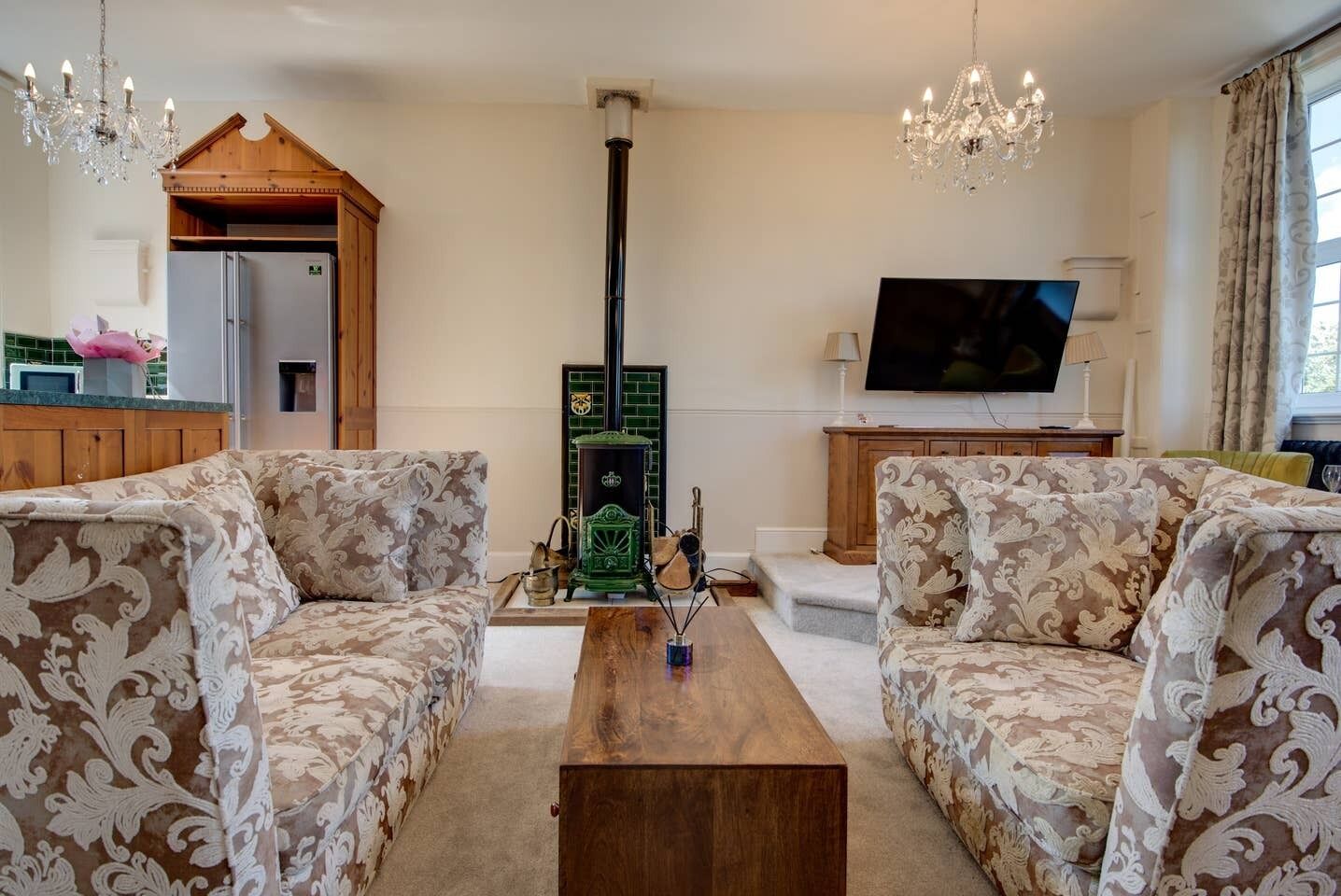 Una sala de estar con dos sofás estampados, una mesa de centro de madera, un televisor y una estufa verde.
